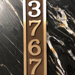 May include: Vertical house number plaque with the numbers 3767 in white and gold on a brown background. The plaque is made of metal and has a brushed finish.