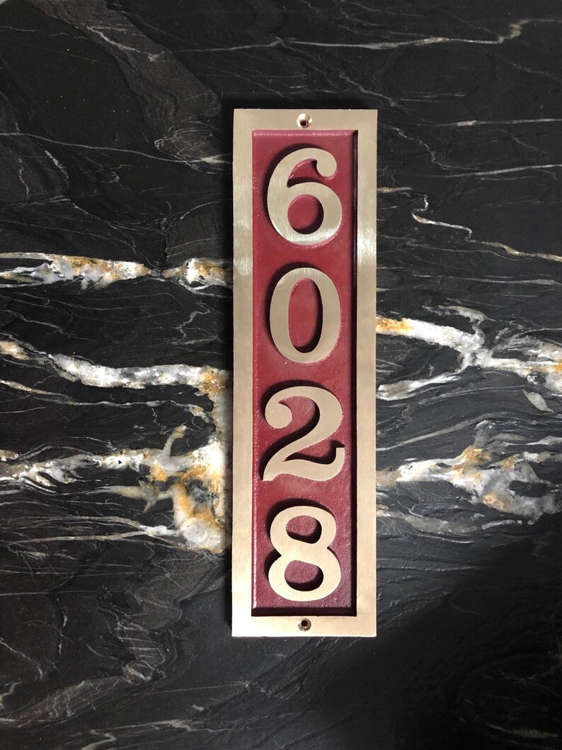 May include: A vertical house number plaque with a burgundy background and gold numbers. The numbers are 6028.