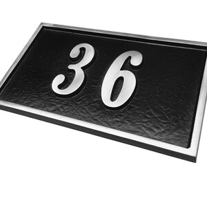 May include: Black house number plaque with a silver border and the number 36 in silver lettering.