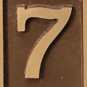 May include: A close-up of a brown plaque with a raised, cream-coloured number "7" on it.