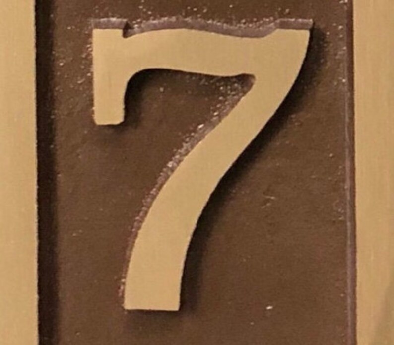 May include: A close-up of a brown plaque with a raised, cream-coloured number "7" on it.