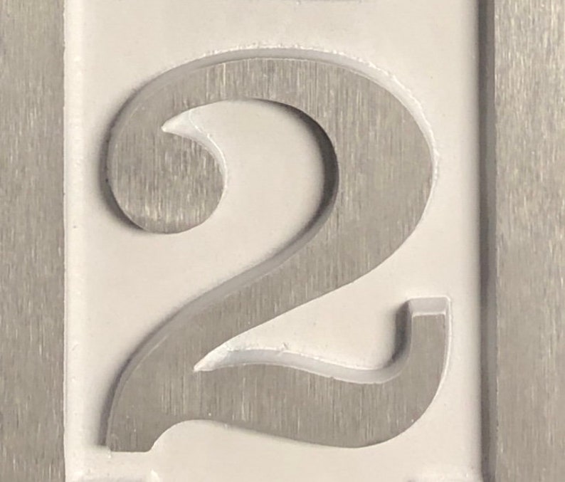 May include: A close-up of a silver metal number two. The number is raised and has a brushed finish.