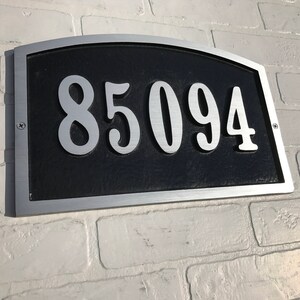 May include: A silver and black house number plaque with the number 85094 in white.