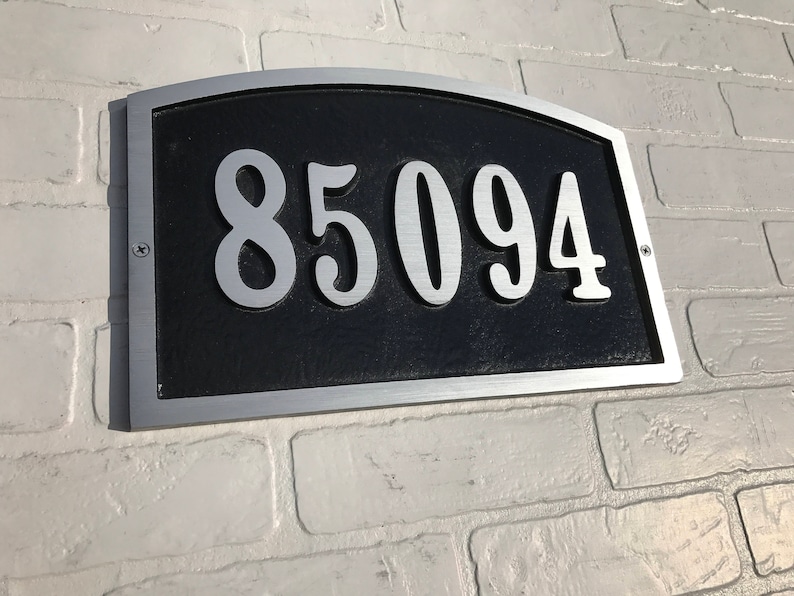 May include: A silver and black house number plaque with the number 85094 in white.