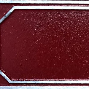 Pu&ograve; includere: Primo piano di un cartello in metallo rosso con bordo argentato. Il cartello ha una superficie testurizzata.