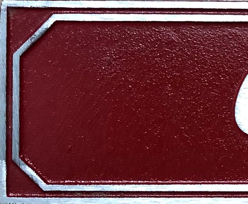 Pu&ograve; includere: Primo piano di un cartello in metallo rosso con bordo argentato. Il cartello ha una superficie testurizzata.