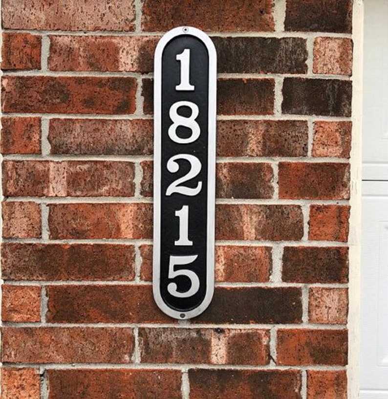May include: A black and silver vertical house number sign with the number 18215 printed in white.