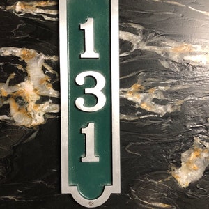 May include: A silver and green house number plaque with the number 131 on it.