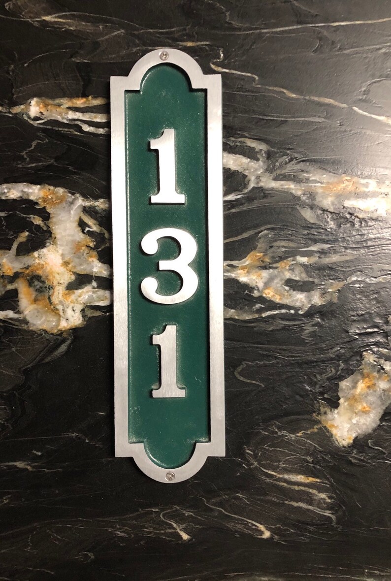 May include: A silver and green house number plaque with the number 131 on it.