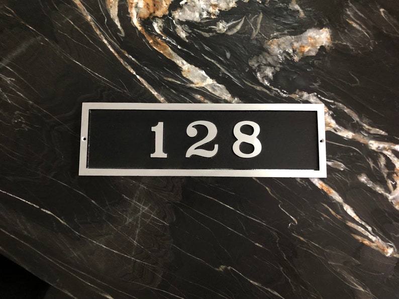 May include: A silver rectangular house number plaque with a black background and the number 128 in white.