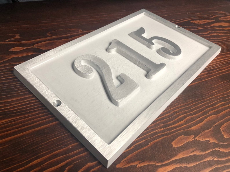 May include: White rectangular house number sign with a silver frame and the number 215 embossed in silver.