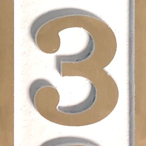 May include: A white number three with a brown outline. The number is on a white background.