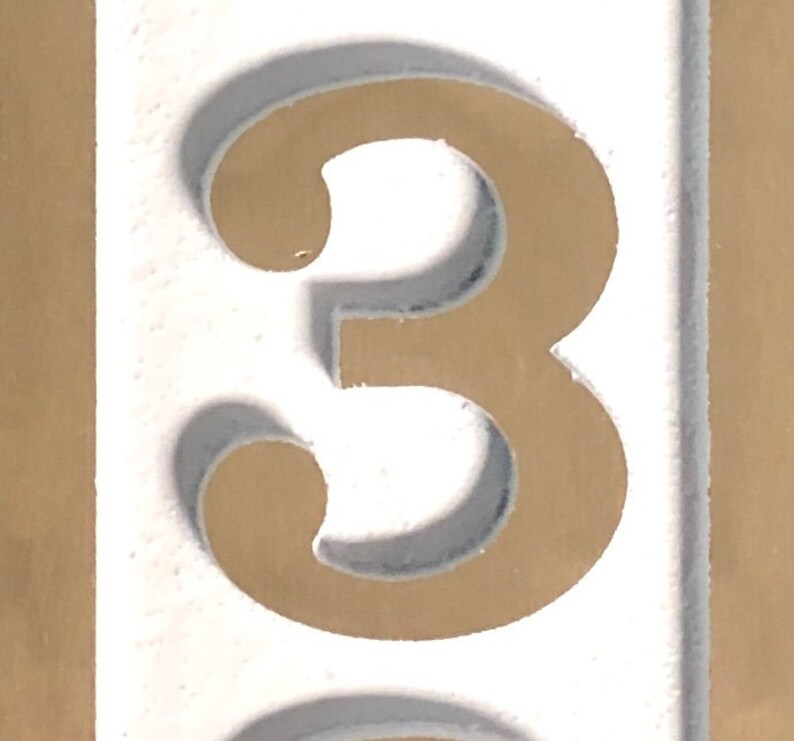 May include: A white number three with a brown outline. The number is on a white background.