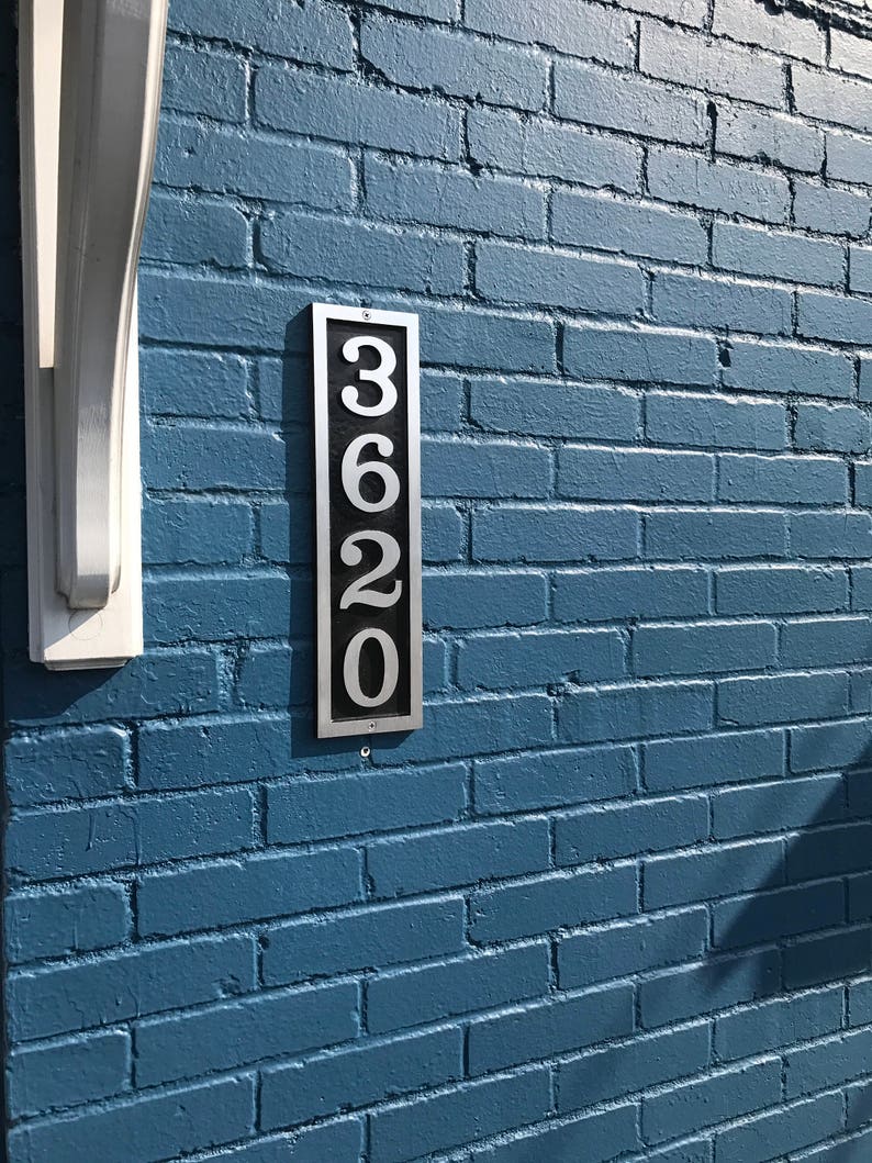Puede incluir: Un letrero de n&uacute;mero de casa de metal plateado con el n&uacute;mero 3620 en una pared de ladrillo azul.