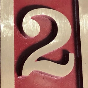 May include: A close-up of a red wooden sign with a white number "2" carved into it. The number is raised and has a shadow effect.