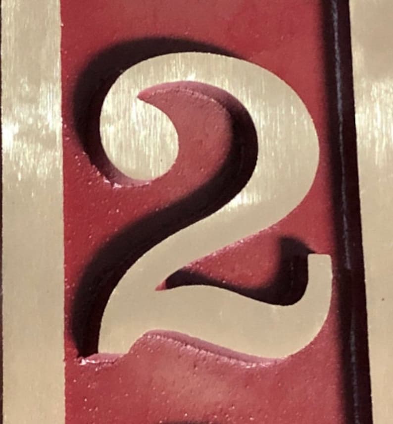 May include: A close-up of a red wooden sign with a white number "2" carved into it. The number is raised and has a shadow effect.