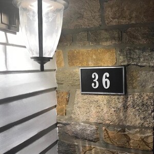 May include: A black and white house number sign with the number 36 on a stone wall.