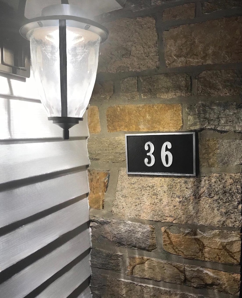 May include: A black and white house number sign with the number 36 on a stone wall.