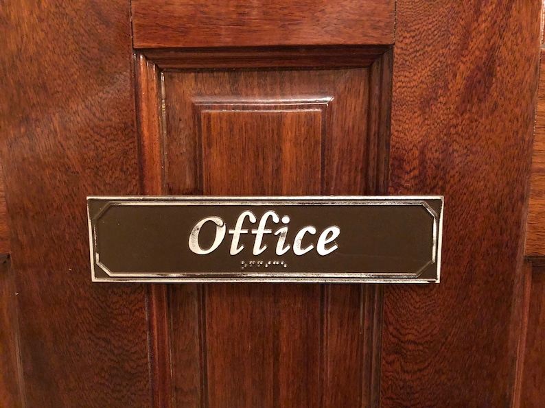 May include: A brown wooden door with a silver plaque that reads "Office" in white lettering. The plaque also has braille lettering.