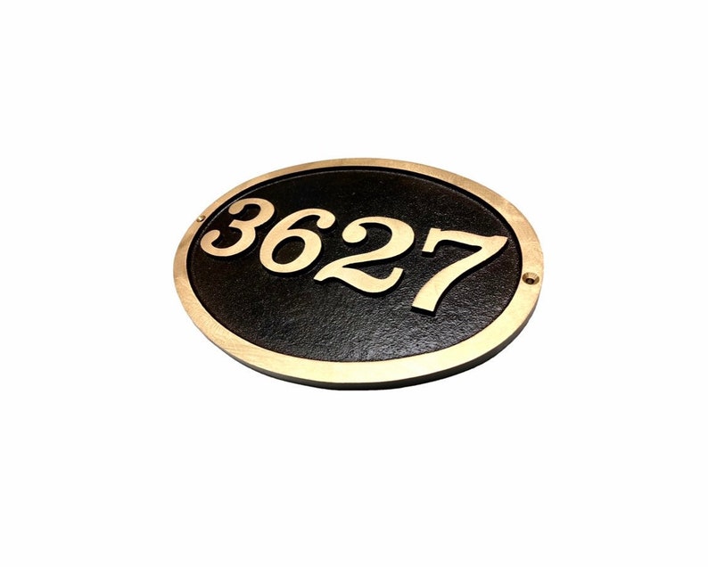 May include: Oval-shaped house number plaque with a black background and gold-coloured numbers. The number 3627 is displayed on the plaque.