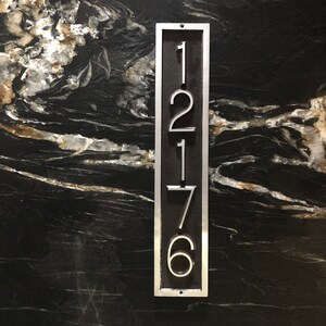 May include: A silver metal house number plaque with the numbers 1276 displayed vertically.