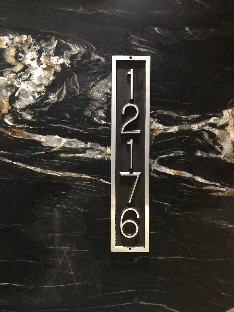 May include: A silver metal house number plaque with the numbers 1276 displayed vertically.