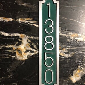 May include: A vertical silver and green house number plaque with the number 13850.