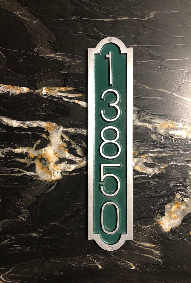 May include: A vertical silver and green house number plaque with the number 13850.
