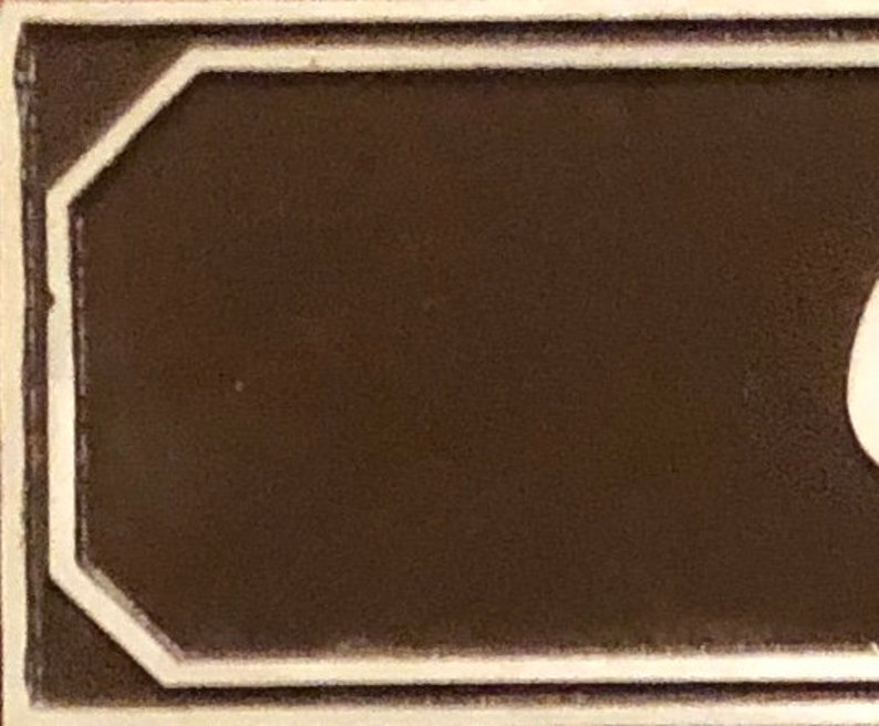 May include: A brown rectangular sign with a white border. The sign has a beveled edge and a slightly textured surface.