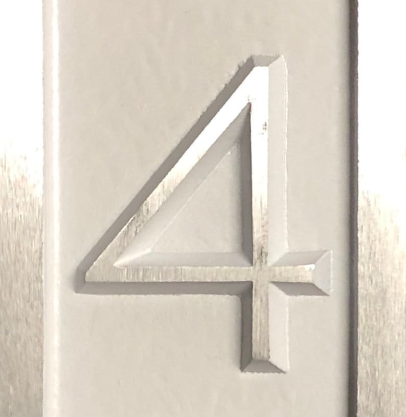 May include: A close-up of a white, rectangular sign with the number "4" embossed in the center. The number is raised and has a slightly textured surface.