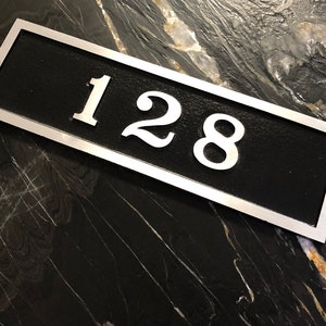 May include: A silver rectangular house number plaque with black background and the number 128 in white.
