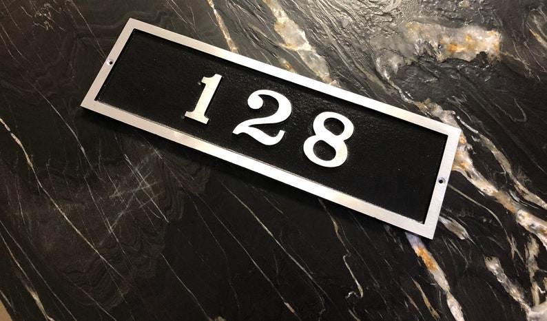May include: A silver rectangular house number plaque with black background and the number 128 in white.