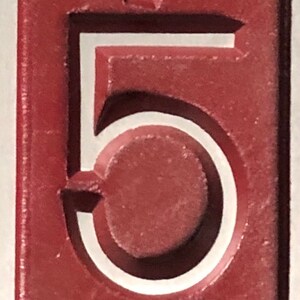 May include: A close-up of a red number five with a white outline. The number is raised and has a textured surface.