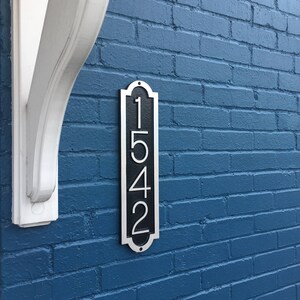 May include: A black and silver house number plaque with the number 1542 on a blue brick wall.