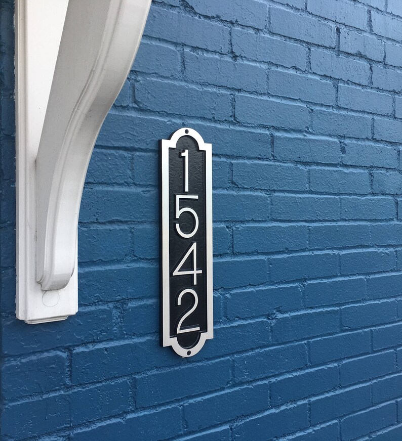 May include: A black and silver house number plaque with the number 1542 on a blue brick wall.