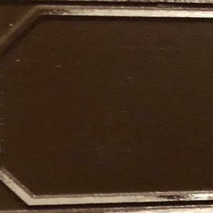 May include: A brown wooden plaque with a silver border. The plaque has a smooth surface and a slightly raised edge.
