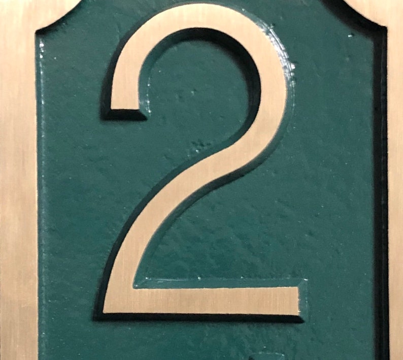 May include: A close-up of a house number plaque with the number "2" in a gold-colored font on a dark green background.