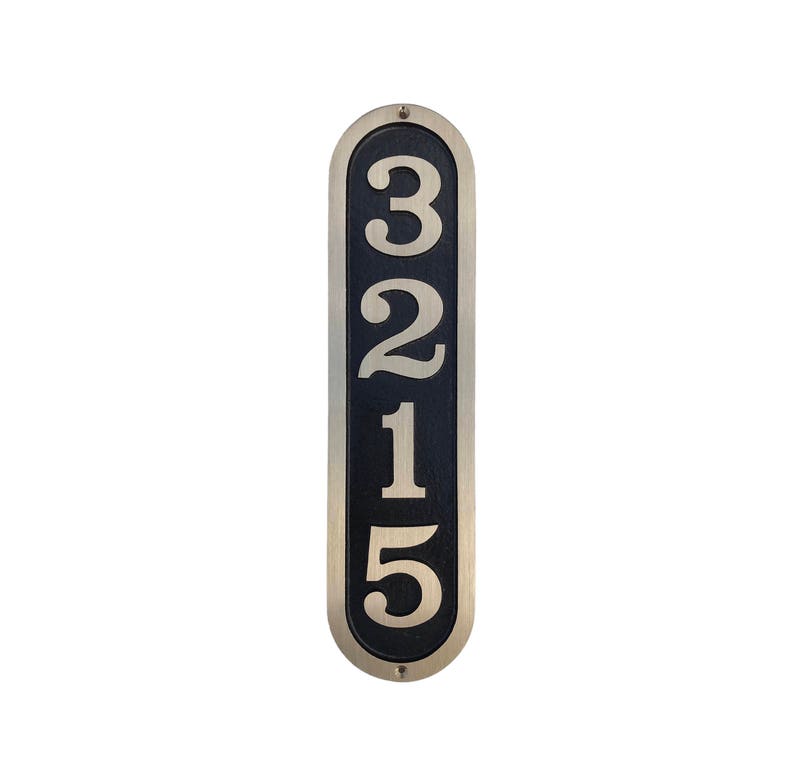 May include: A vertical, oval-shaped house number plaque with a black background and silver numbers. The numbers 3215 are displayed in a vertical line.