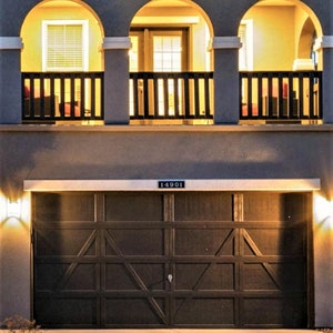 May include: Exterior view of a two-story house at dusk. The house features a dark brown garage door, a balcony with arched openings, and a light-colored exterior. The address "14901" is displayed above the garage.