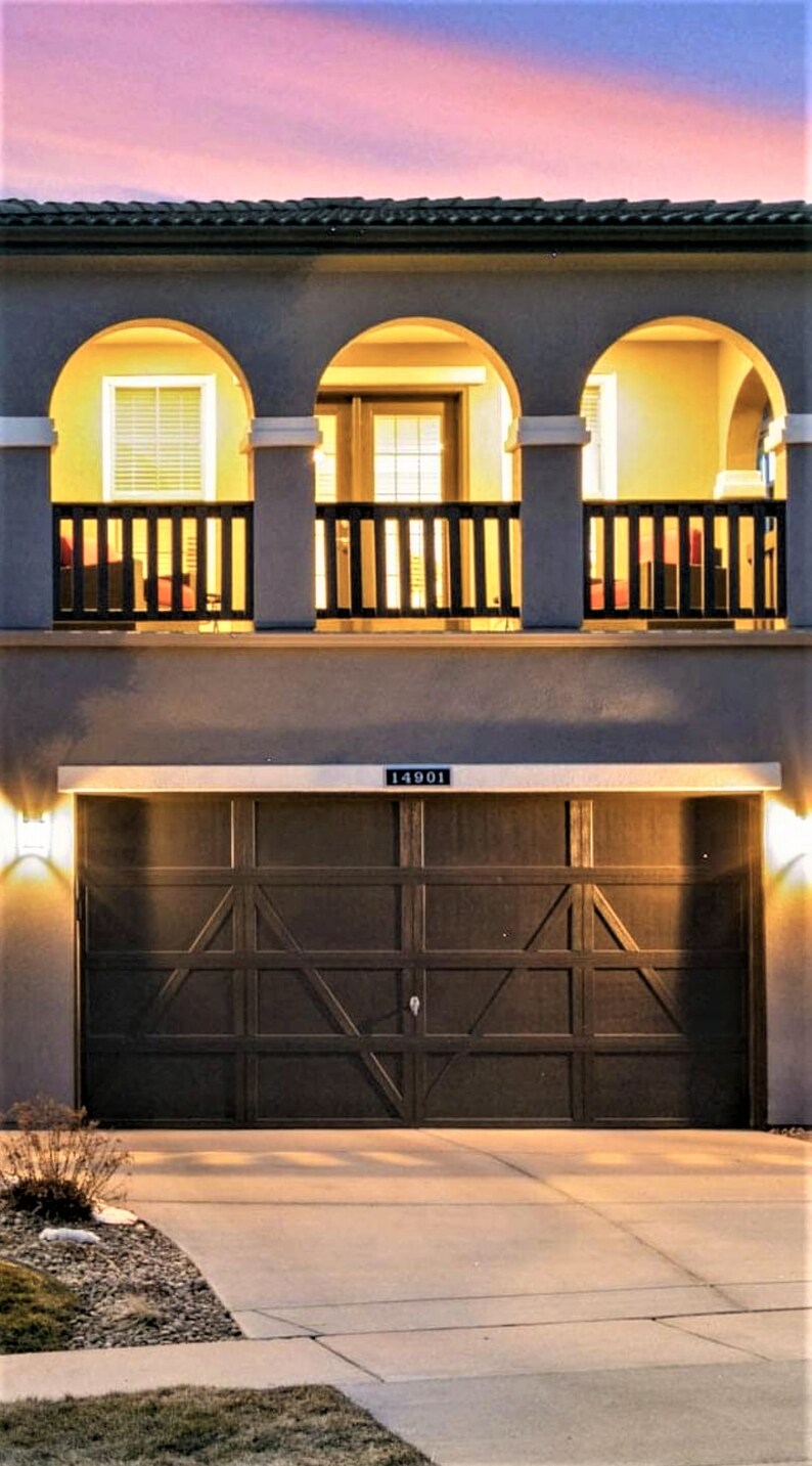May include: Exterior view of a two-story house at dusk. The house features a dark brown garage door, a balcony with arched openings, and a light-colored exterior. The address "14901" is displayed above the garage.
