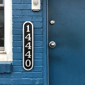 May include: A blue brick building with a blue door. The door has a silver door handle and a silver doorbell. A black and silver plaque with the number 1440 is attached to the brick wall.