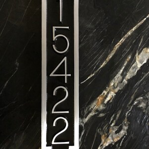 May include: A vertical silver metal house number sign with black background and the numbers 15422.