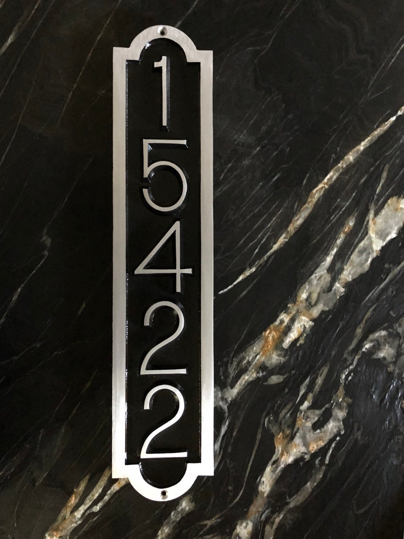 May include: A vertical silver metal house number sign with black background and the numbers 15422.