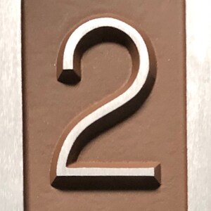 May include: A close-up of a silver number "2" embossed on a brown background.