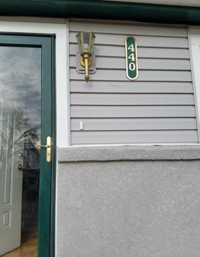 May include: A green door with a glass panel and a gold door handle. A gold light fixture is mounted on the wall next to the door. A green plaque with the number 440 is mounted on the wall.