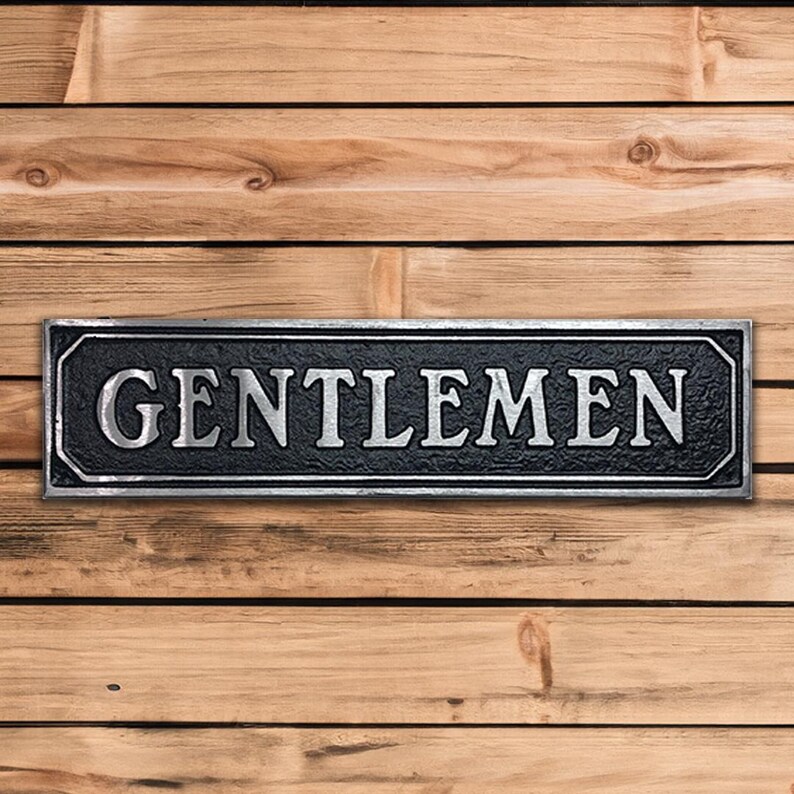 May include: A black and silver metal sign with the word "GENTLEMEN" in raised silver letters.