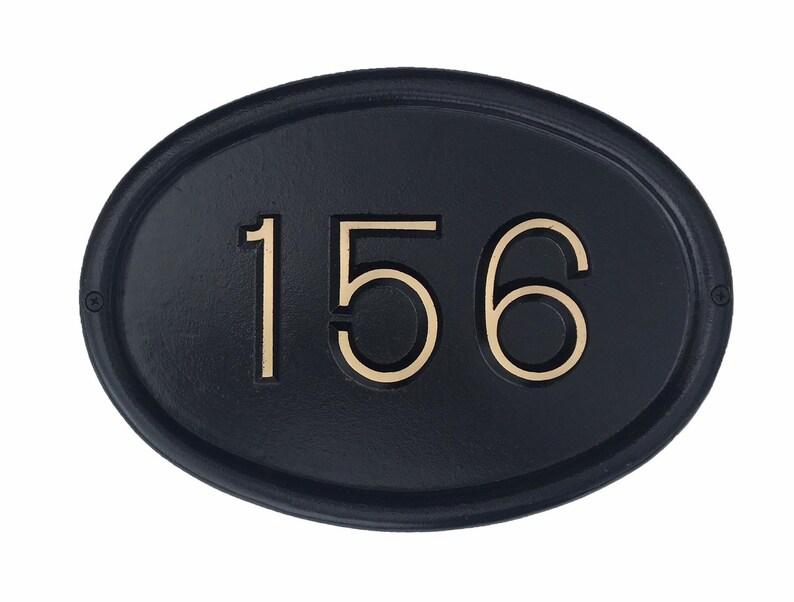 May include: Black oval-shaped house number plaque with gold-colored numbers "156" embossed on the surface.