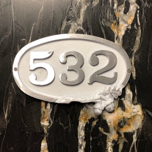 May include: White oval-shaped house number sign with silver numbers "532" on a black background.