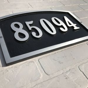 May include: A silver and black house number plaque with the number 85094 in large, silver, stylised lettering.