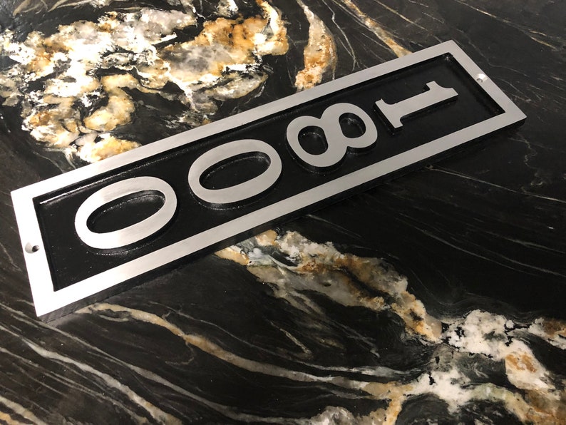 Puede incluir: Un letrero de n&uacute;mero de casa de metal plateado con fondo negro y el n&uacute;mero 0081 en letras plateadas en relieve.
